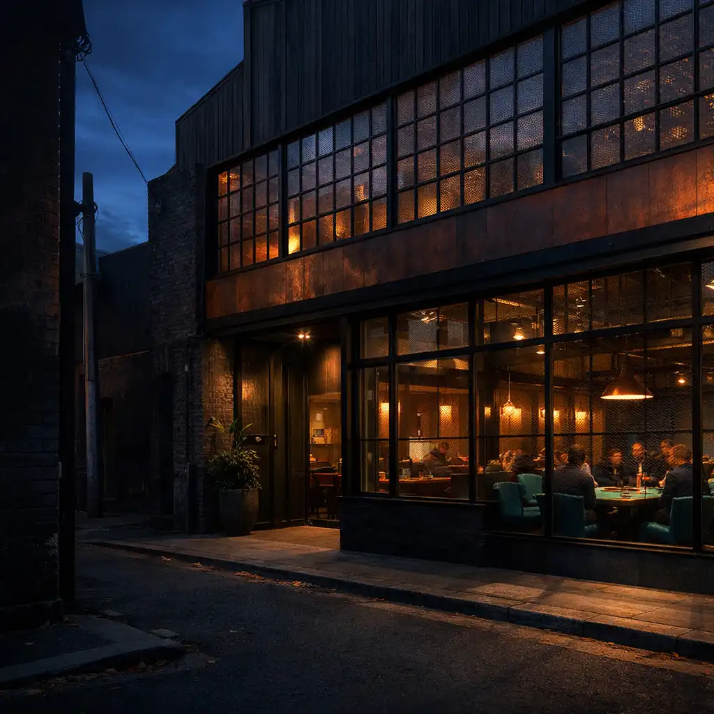 Dusk view of TheGalleryTable's industrial Fitzroy exterior, with warm restaurant tables and card spaces visible through the windows.
